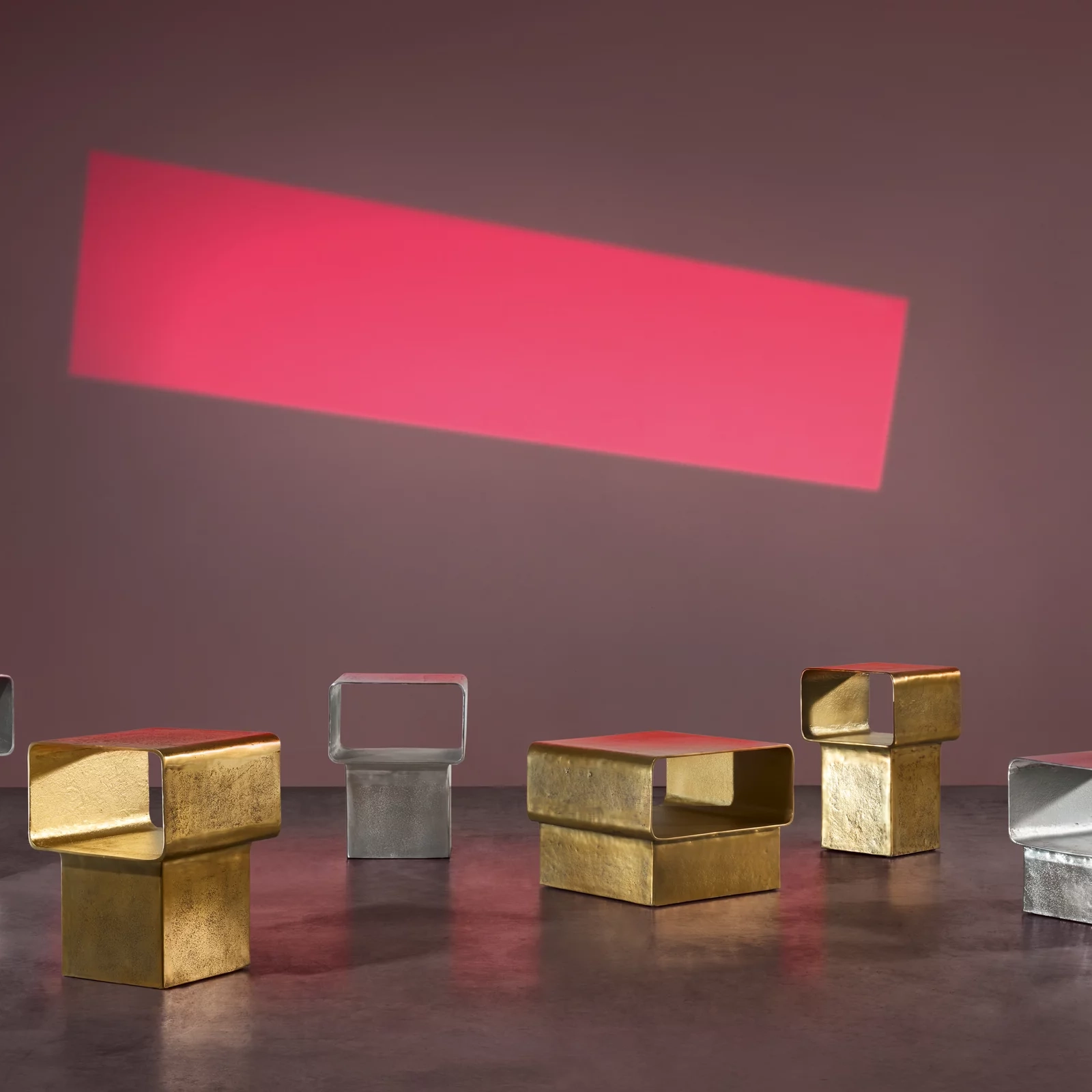 Moderne Szene mit goldenen und silbernen Metallhockern vor rotem Lichtstreifen auf Betonboden.