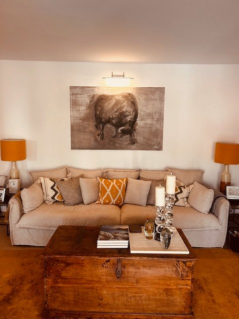 Gemütliches Wohnzimmer mit beigem Sofa, Erdtönen, rustikalem Holztisch und Tiergemälde an der Wand.