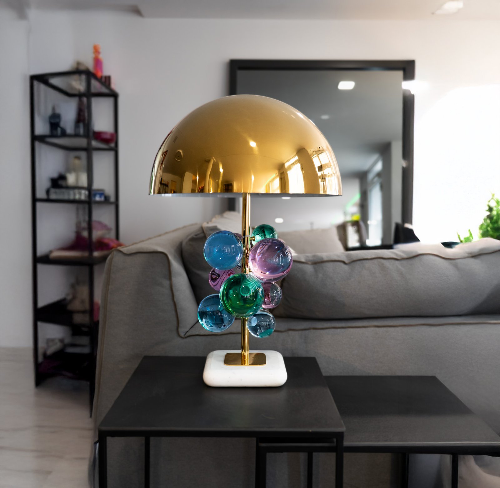 Moderne Tischlampe mit goldenem Schirm und bunten Glaskugeln auf dunklem Tisch in stilvollem Raum.