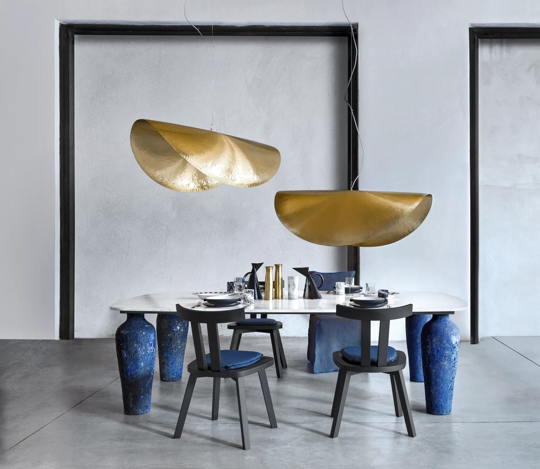 Moderner Essbereich mit ovalem Tisch auf blauen Vasen, goldenen Lampen und schwarzen Stühlen.