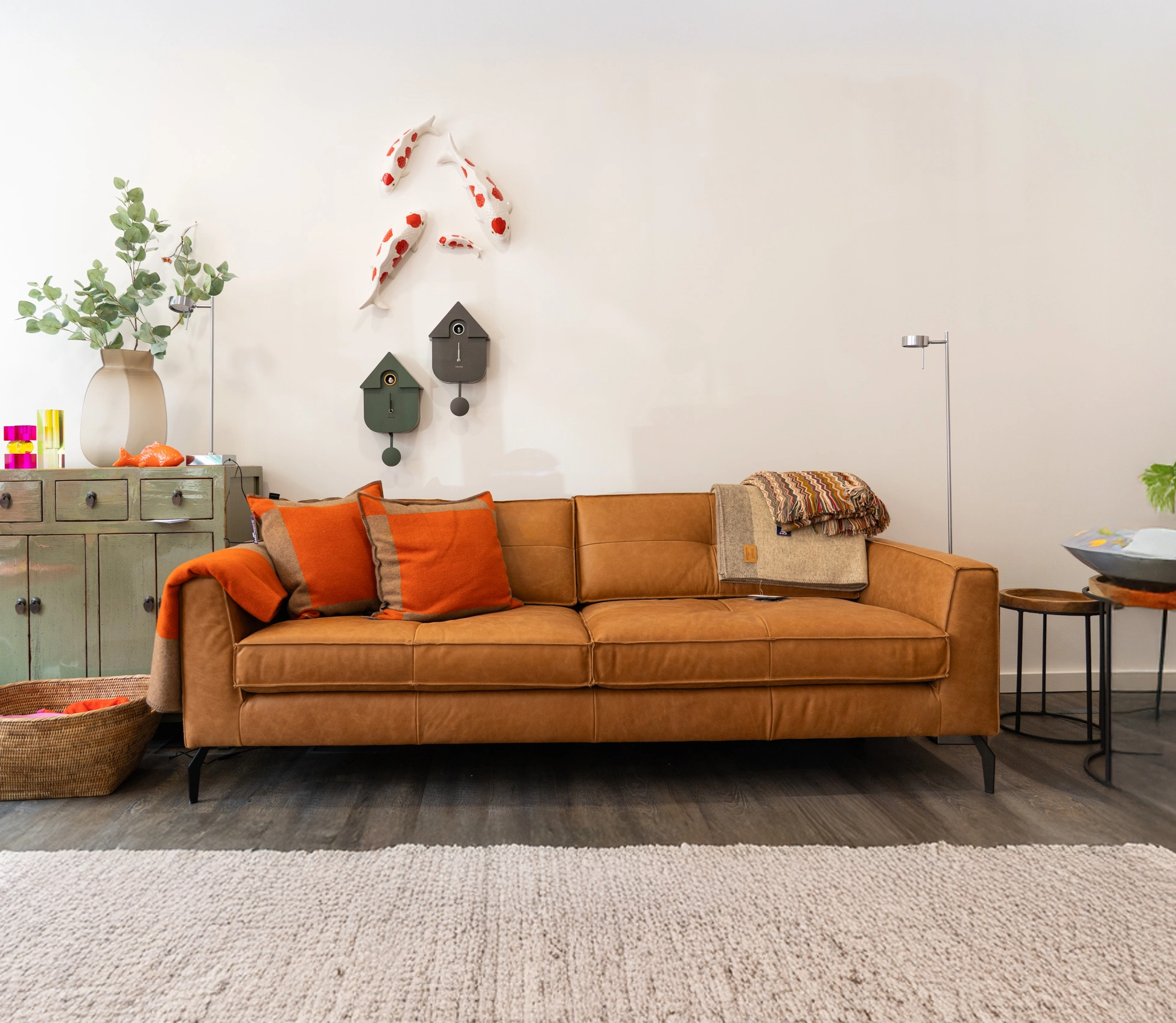 Ein stilvolles Wohnzimmer mit braunem Ledersofa, grünen Sideboard und dekorativen Wandobjekten.