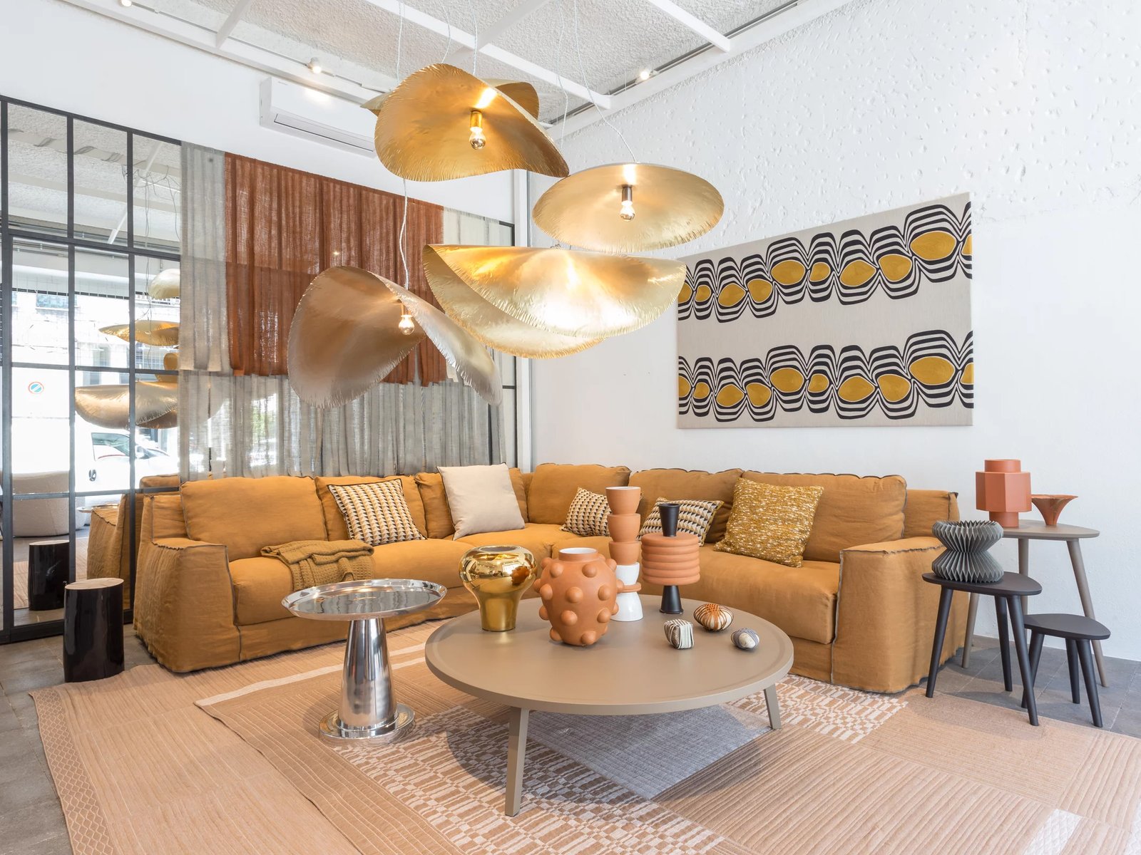 Modernes Wohnzimmer mit beiger Couch, rundem Tisch, goldener Leuchte und geometrischem Wandteppich.