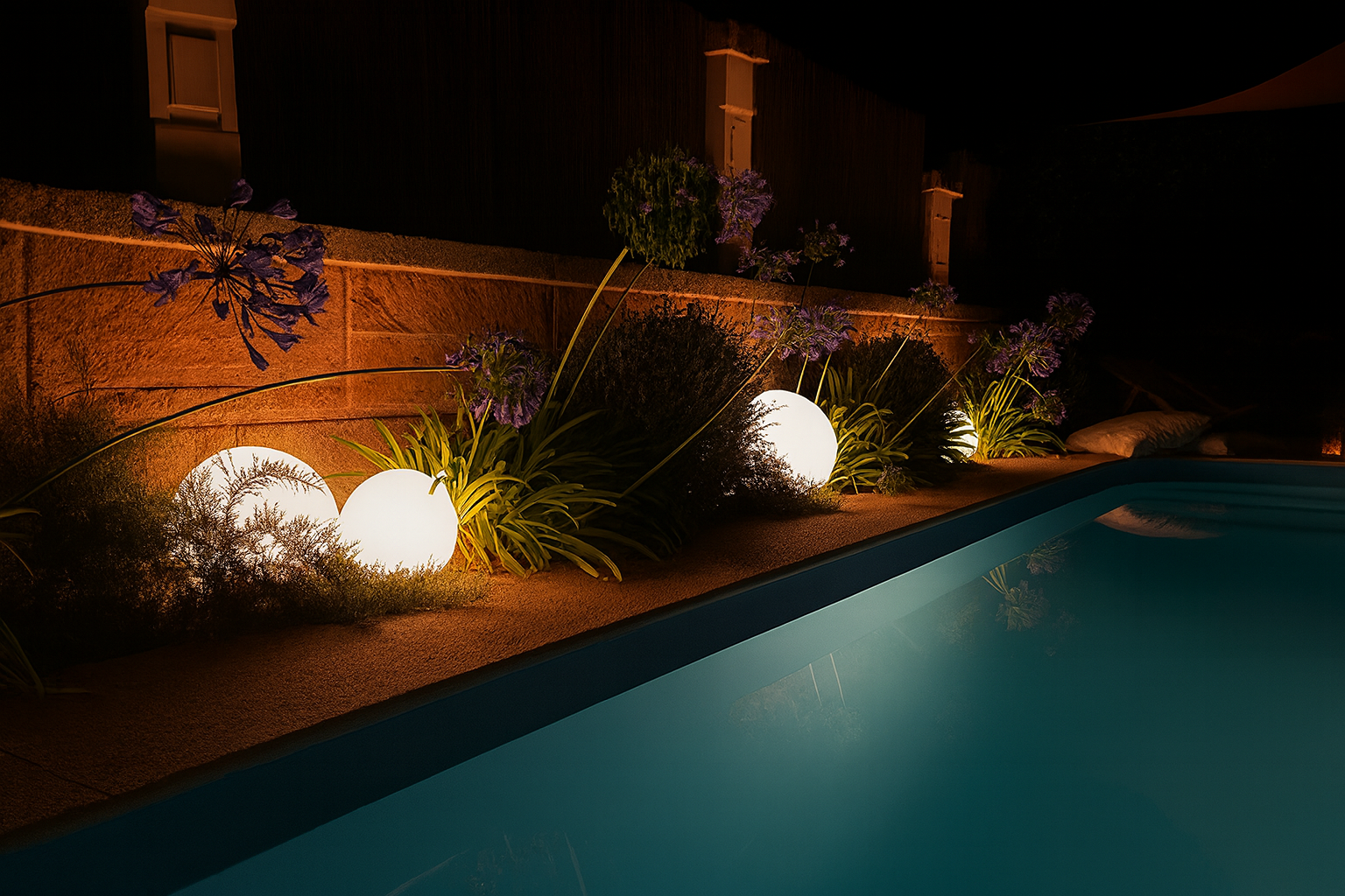 Ein beleuchteter Pool in einem nächtlichen Garten, umgeben von Kugelleuchten und lila blühenden Pflanzen.